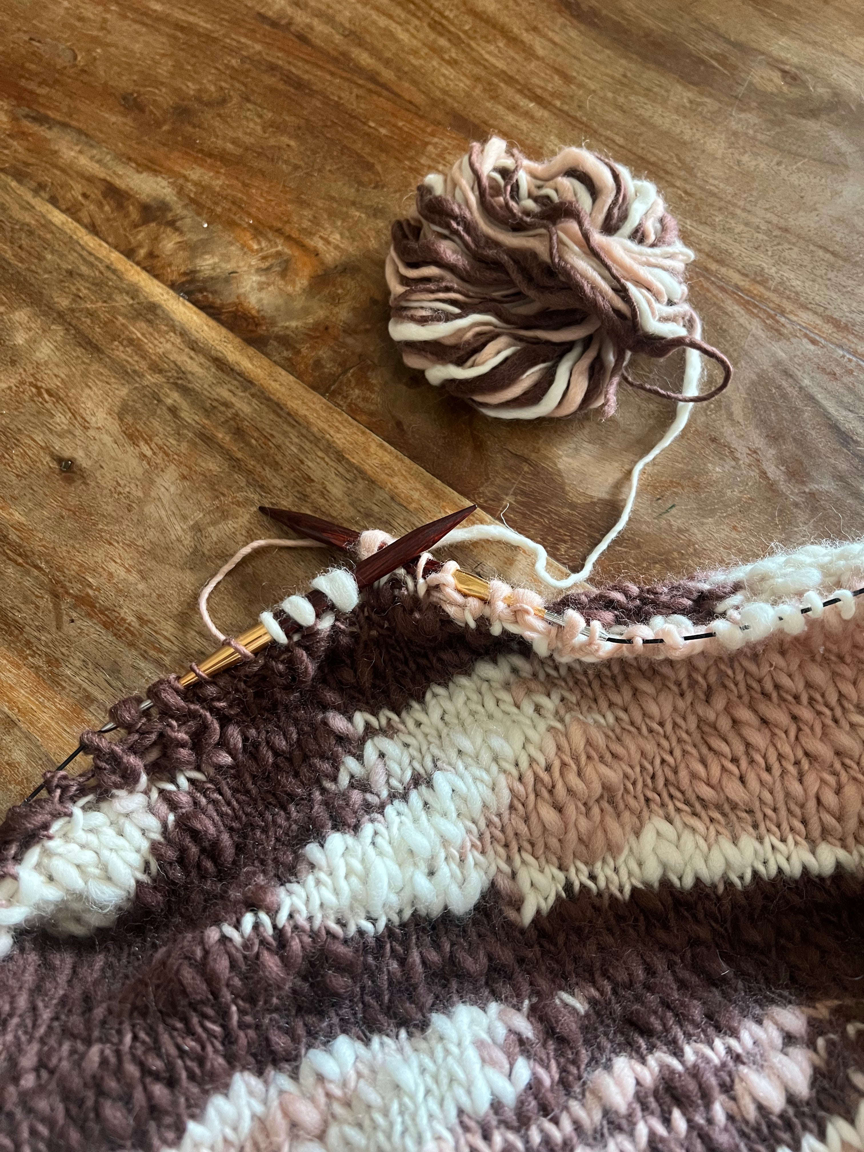 Dettaglio di una maglia fatta a mano con lana naturale multicolore, filato artigianale lavorato a ferri su superficie in legno